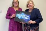 Jane with a representative from Mesothelioma UK holding a 'Don't let the Dust Settle' board